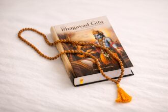 Geschlossene Bhagavad Gita mit Mala aus Holzperlen auf hellem Hintergrund