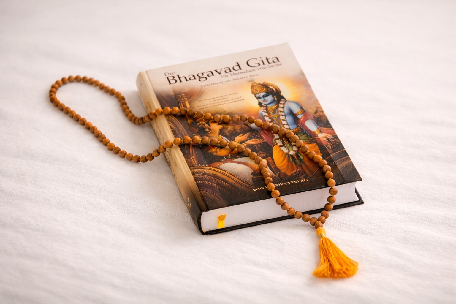 Geschlossene Bhagavad Gita mit Mala aus Holzperlen auf hellem Hintergrund