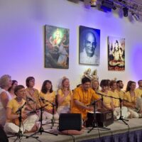 Gruppe von Menschen beim Satsang und Kirtan auf der Bühne im Yoga Vidya Ashram, mit spirituellen Bildern und Jesusbild im Hintergrund