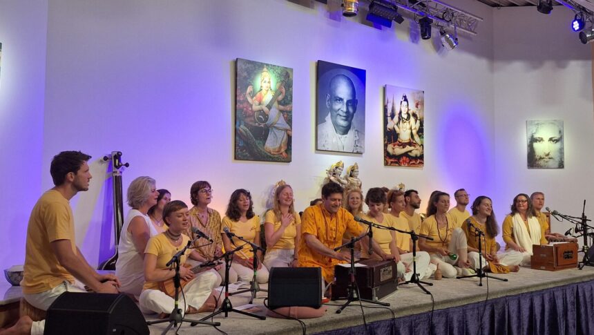 Gruppe von Menschen beim Satsang und Kirtan auf der Bühne im Yoga Vidya Ashram, mit spirituellen Bildern und Jesusbild im Hintergrund